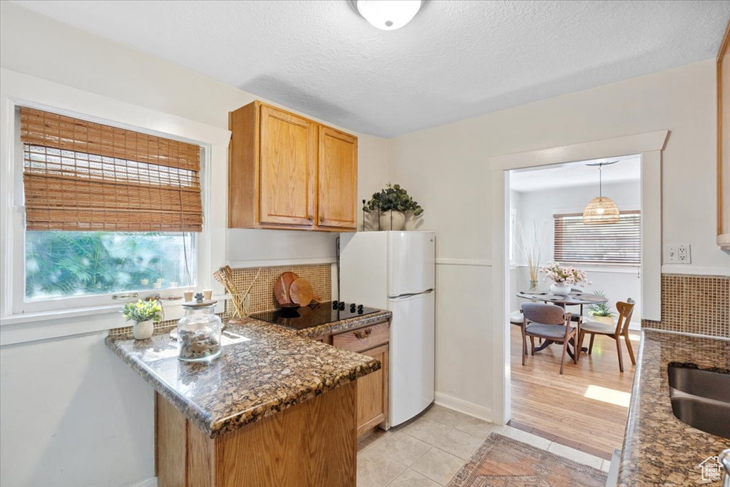 Kitchen featuring freestanding refrigerator, light tile patterned flooring, dark stone counters, a peninsula, and black electric stovetop