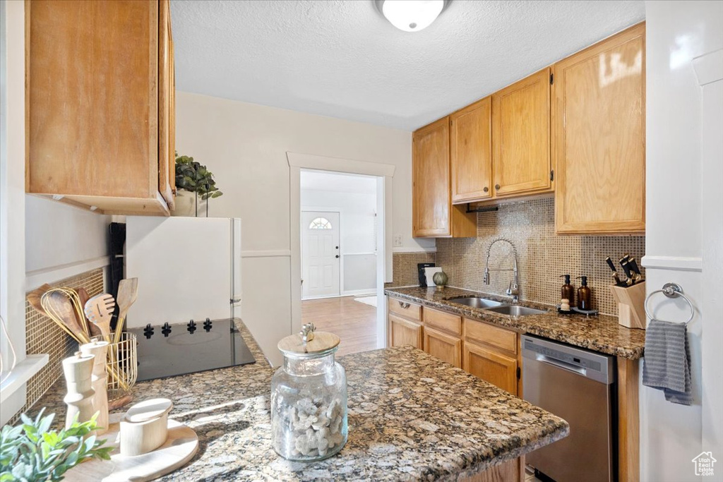 Kitchen featuring dishwasher, backsplash, dark stone countertops, black electric cooktop, and a textured ceiling