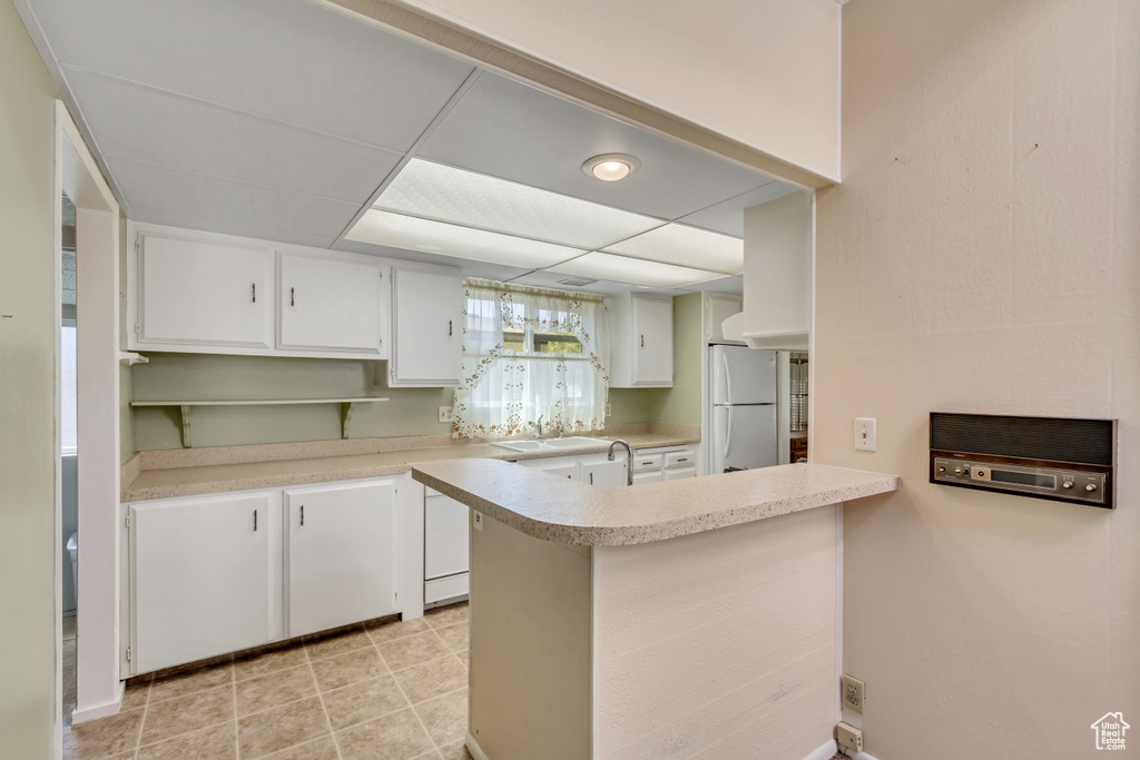Kitchen featuring freestanding refrigerator, light countertops, white cabinets, and a peninsula