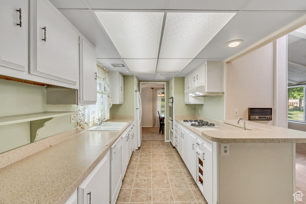 Kitchen featuring white appliances, light countertops, under cabinet range hood, and white cabinetry