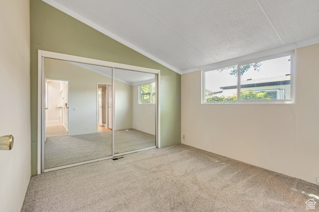 Unfurnished bedroom with carpet flooring, vaulted ceiling, a closet, and a textured ceiling