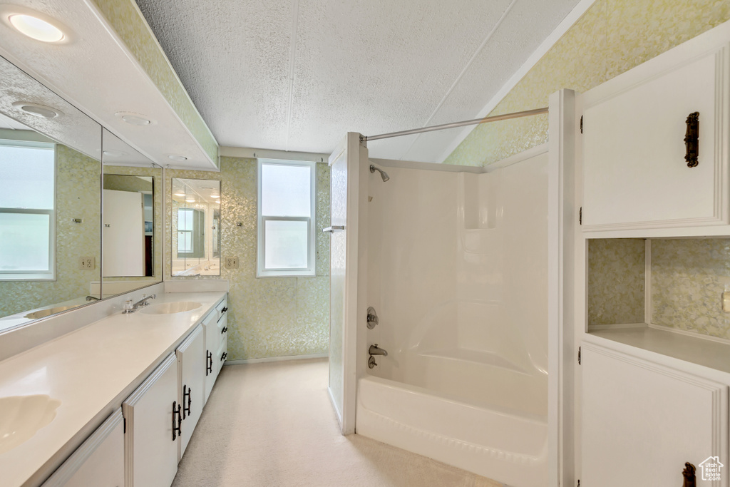 Bathroom featuring a textured ceiling, double vanity, tub / shower combination, and wallpapered walls