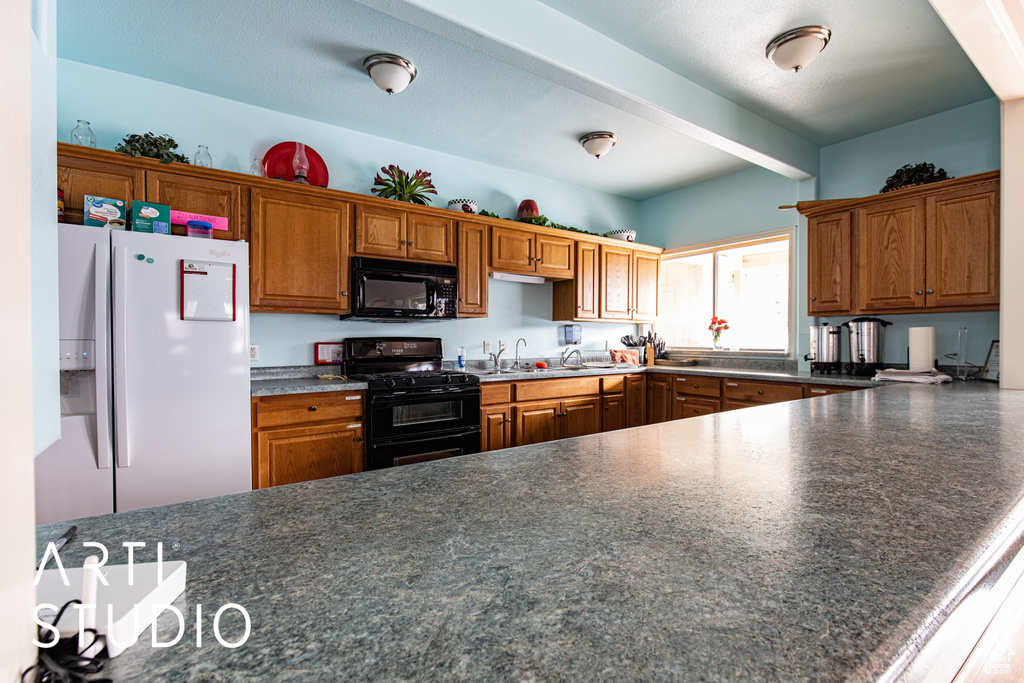 Kitchen featuring black appliances, dark countertops, brown cabinetry, and a peninsula
