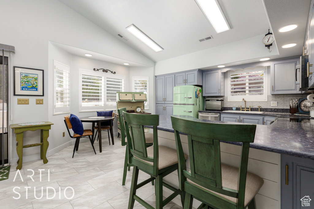 Kitchen with freestanding refrigerator, dark countertops, gray cabinetry, lofted ceiling, and decorative backsplash