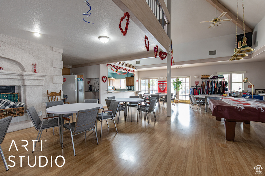 Dining room with light wood-type flooring, a ceiling fan, a multi sided fireplace, beamed ceiling, and pool table