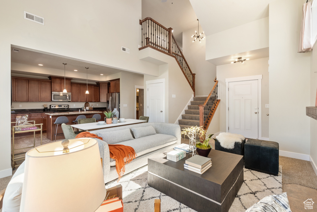 Living area with a high ceiling, stairway, light colored carpet, and a chandelier