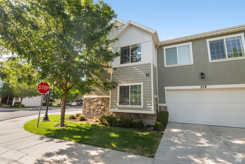 View of property with stone siding, driveway, a garage, and a front yard