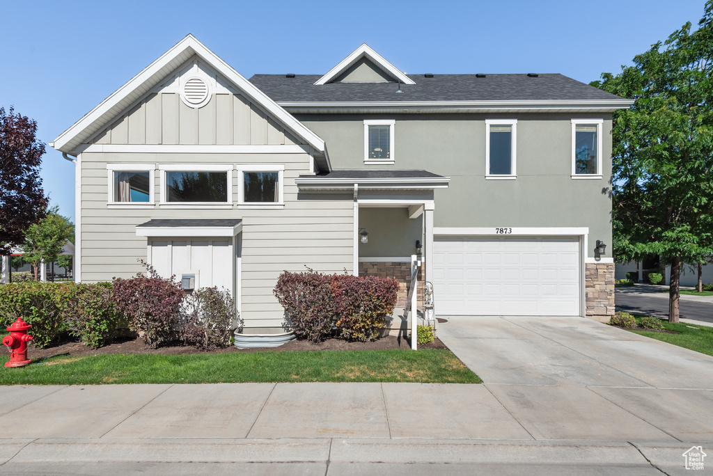 View of front of home featuring stone siding, board and batten siding, driveway, a garage, and roof with shingles