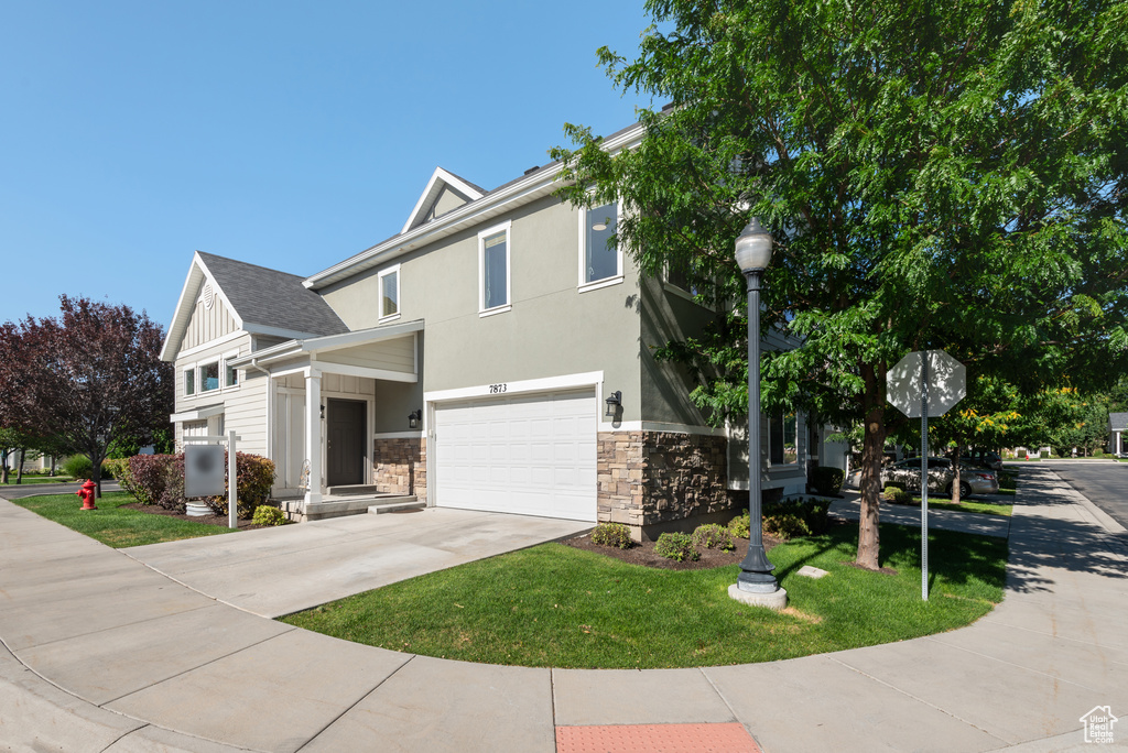 View of front facade featuring stone siding, an attached garage, concrete driveway, a front lawn, and stucco siding
