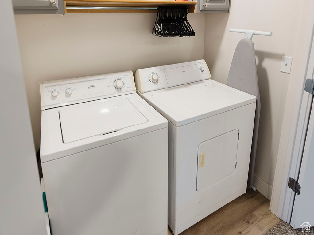 Laundry area featuring washing machine and clothes dryer, cabinet space, and light wood-type flooring