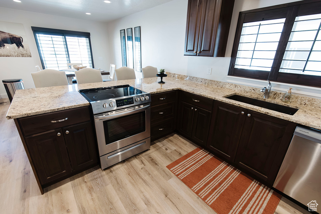 Kitchen featuring stainless steel appliances, light wood-type flooring, a peninsula, light stone counters, and recessed lighting