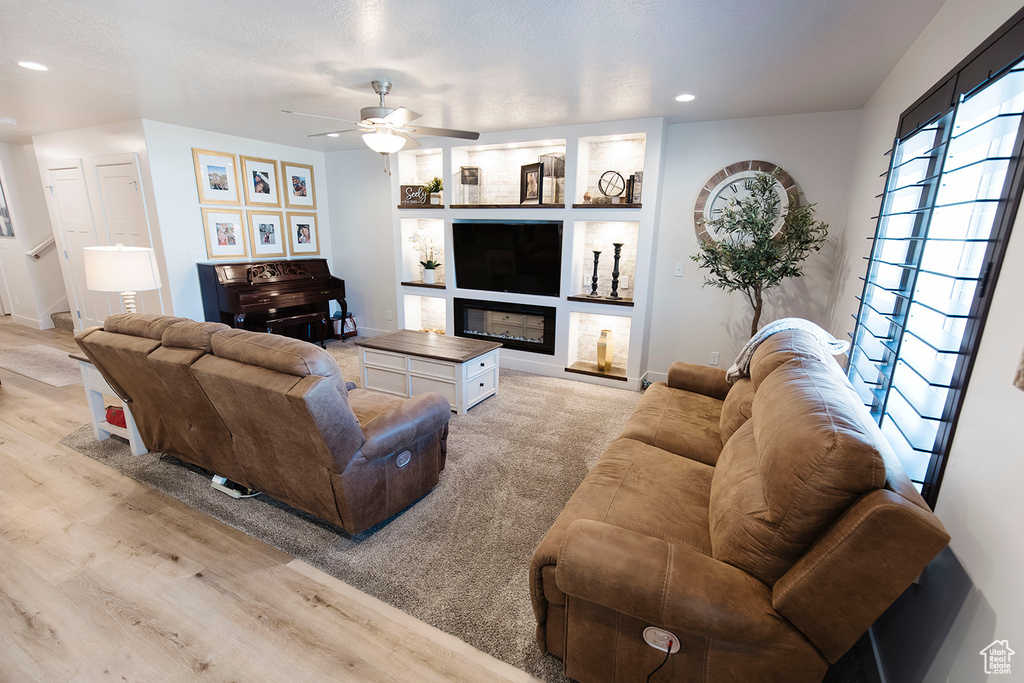 Living area featuring recessed lighting, light wood-style flooring, ceiling fan, a glass covered fireplace, and built in shelves