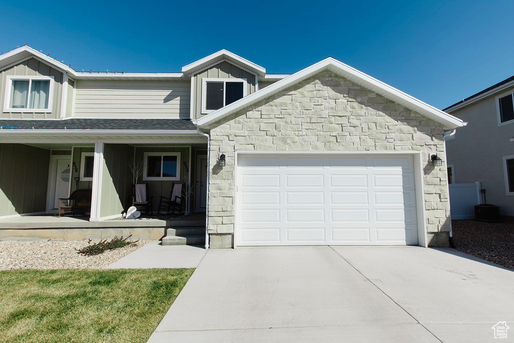 View of front of home with covered porch, driveway, board and batten siding, stone siding, and an attached garage