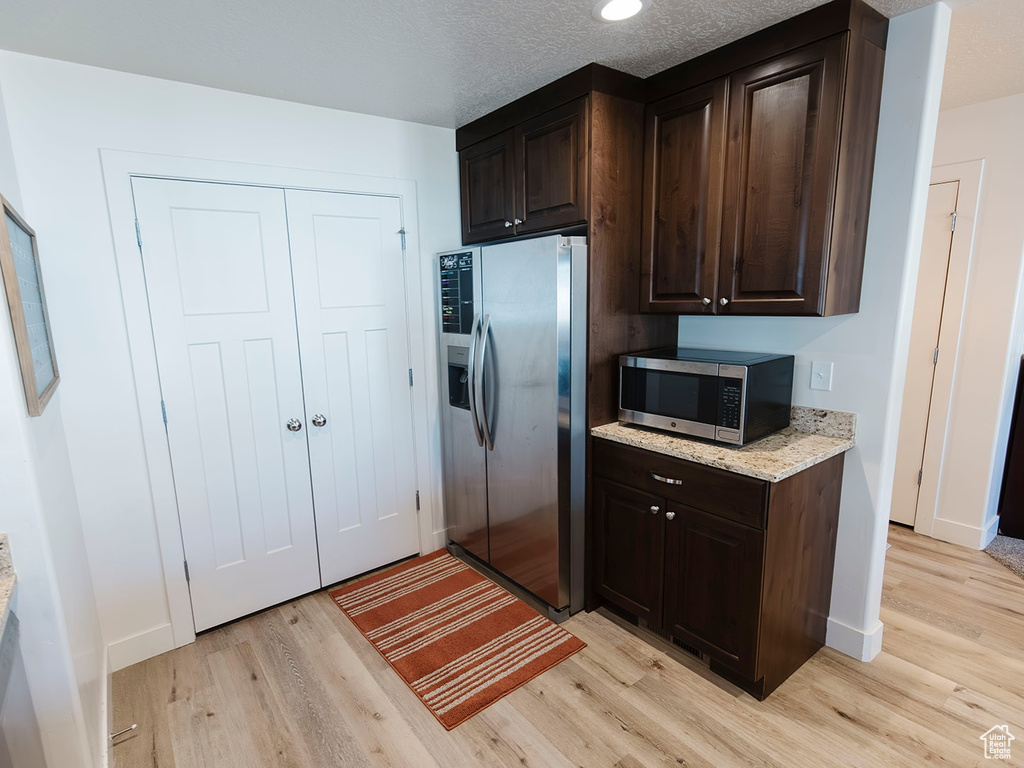 Kitchen featuring appliances with stainless steel finishes, light wood-style flooring, and dark brown cabinetry