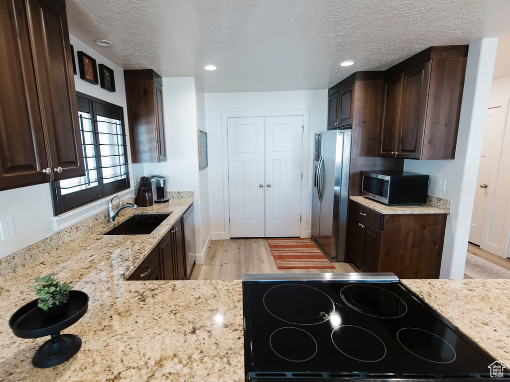 Kitchen featuring stainless steel appliances, dark brown cabinetry, light wood-type flooring, light stone counters, and a textured ceiling