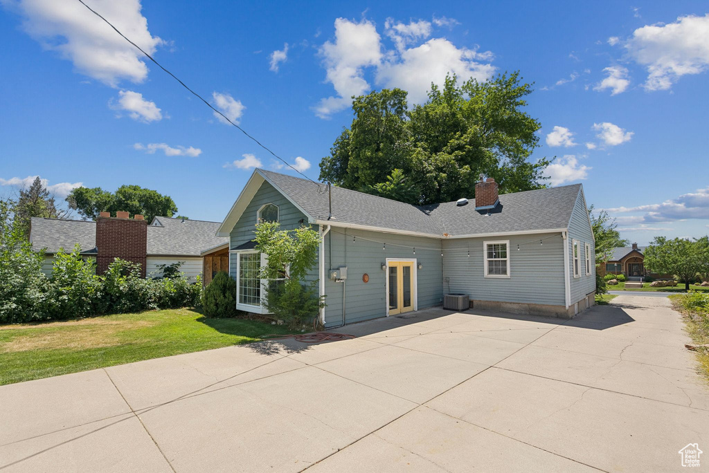 View of front facade featuring driveway, a front lawn, a chimney, roof with shingles, and a patio