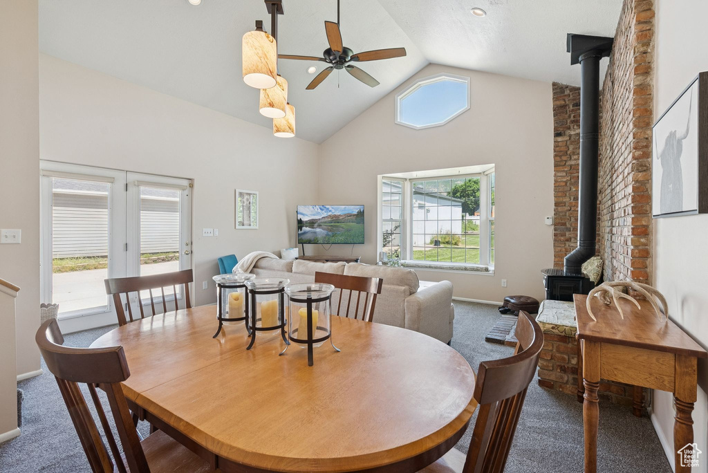 Dining space featuring a wood stove, carpet, a ceiling fan, healthy amount of natural light, and high vaulted ceiling