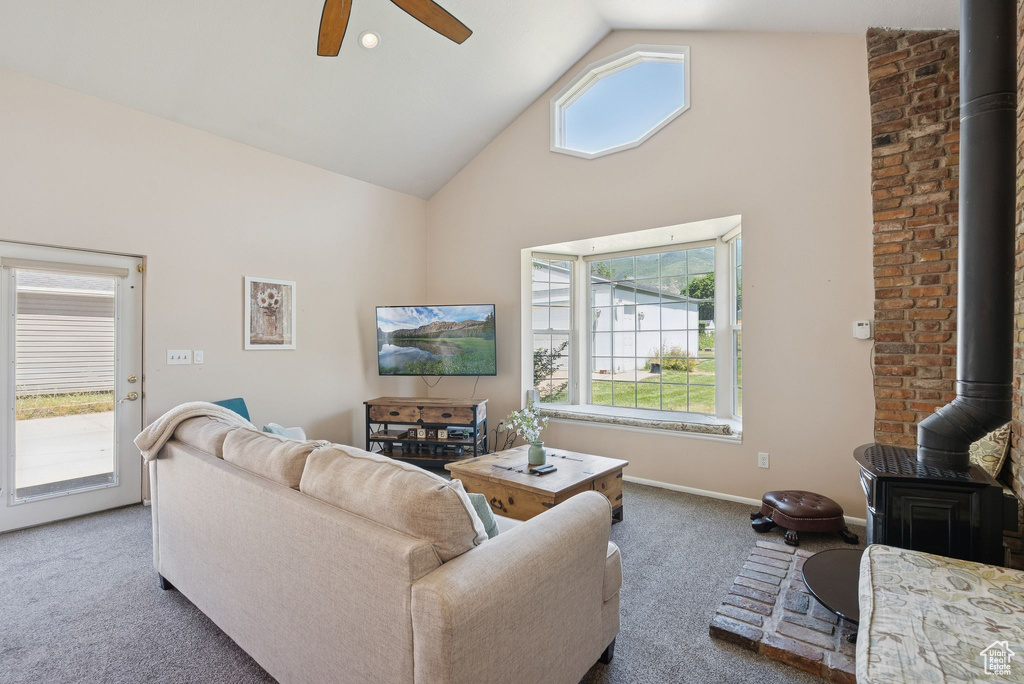 Carpeted living area with a wood stove, high vaulted ceiling, a ceiling fan, and healthy amount of natural light