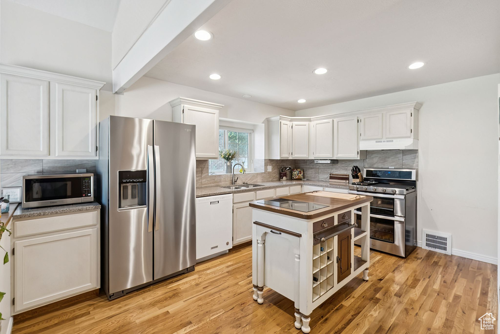 Kitchen featuring appliances with stainless steel finishes, under cabinet range hood, backsplash, white cabinetry, and recessed lighting