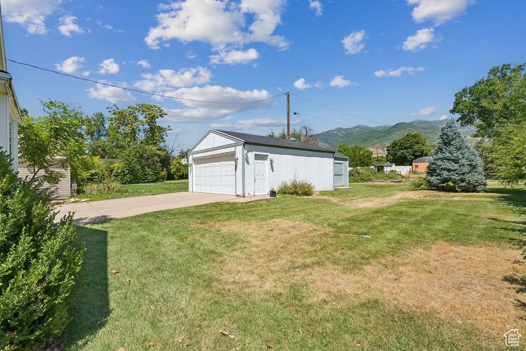 View of green lawn with a detached garage, a mountain view, and an outbuilding