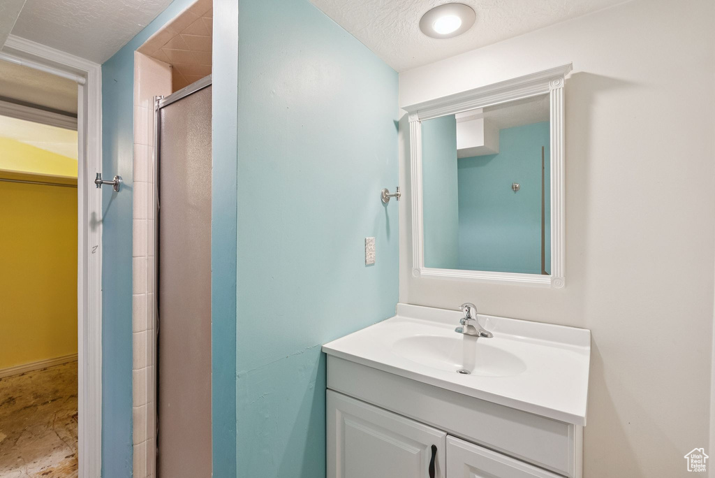 Bathroom featuring a stall shower, vanity, a spacious closet, and a textured ceiling