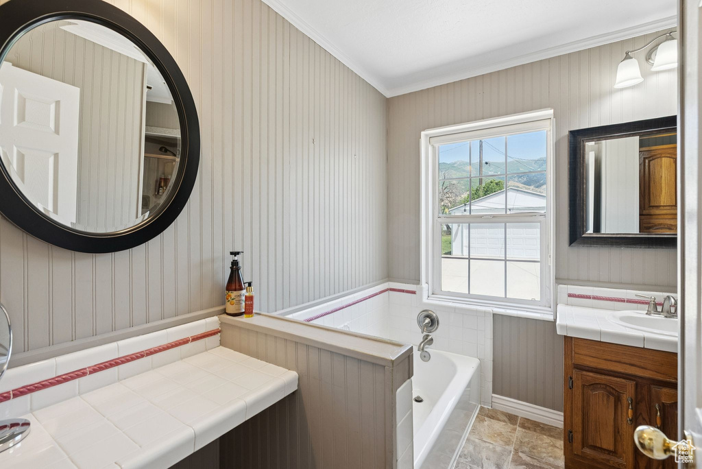 Full bath featuring a garden tub, vanity, ornamental molding, stone finish floors, and wallpapered walls