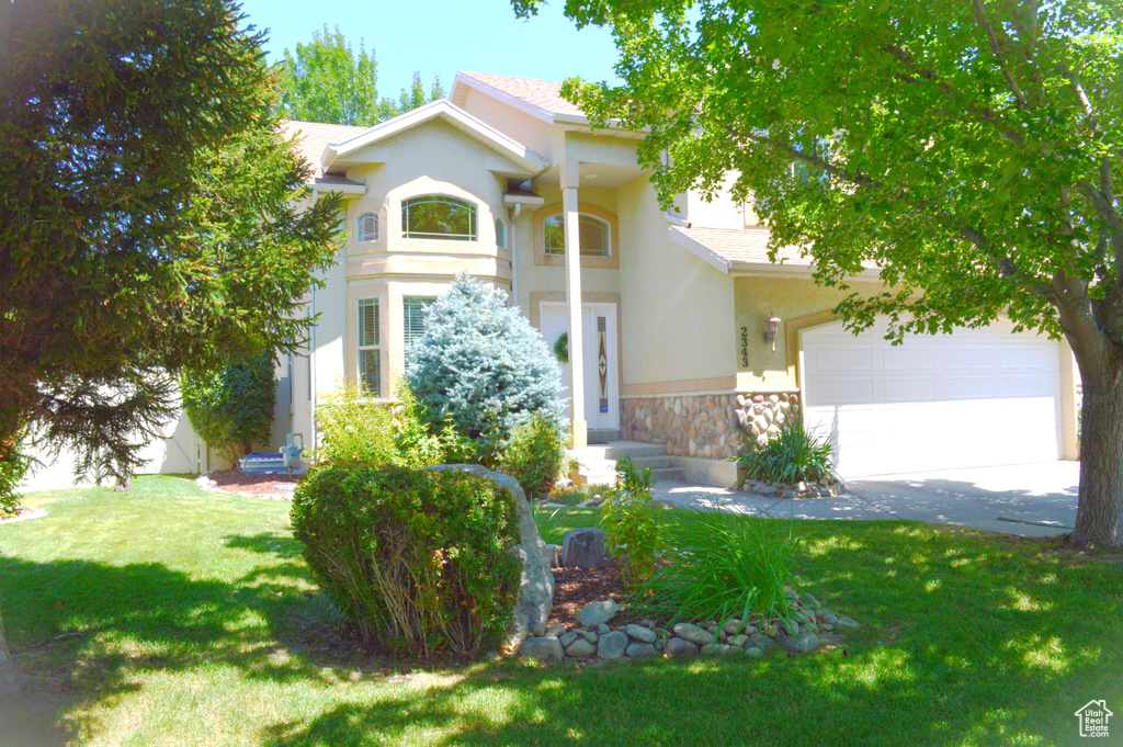 View of front of property featuring stucco siding, a front lawn, stone siding, an attached garage, and driveway