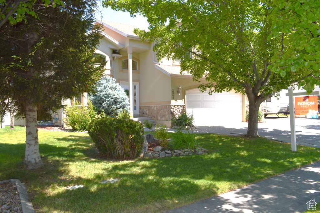 View of front facade with stucco siding, stone siding, a front lawn, and driveway