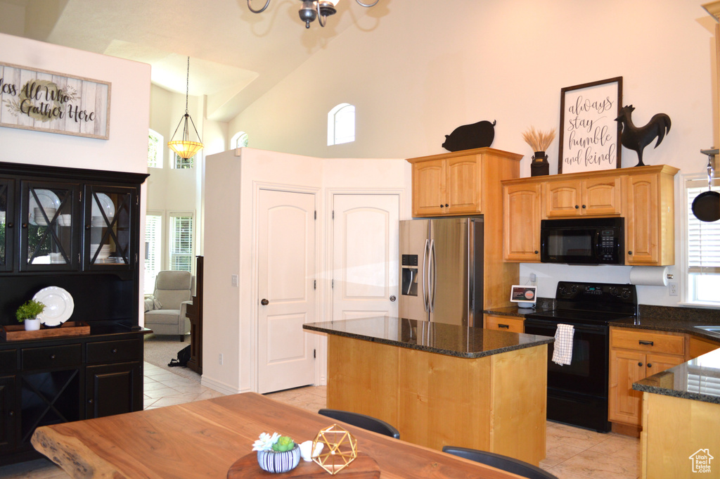 Kitchen with black appliances, high vaulted ceiling, light tile patterned floors, dark stone counters, and a chandelier