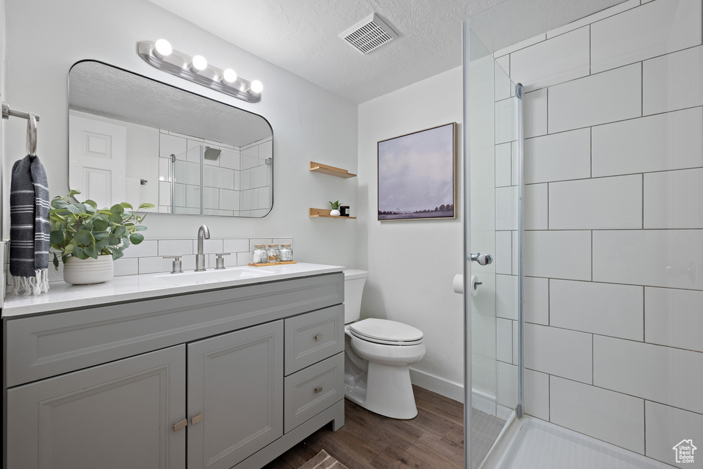 Full bathroom featuring vanity, wood finished floors, tiled shower, tasteful backsplash, and a textured ceiling