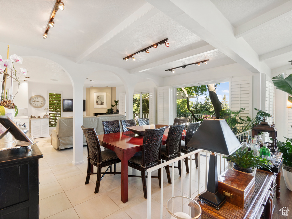 Dining space with rail lighting, arched walkways, light tile patterned floors, and beam ceiling