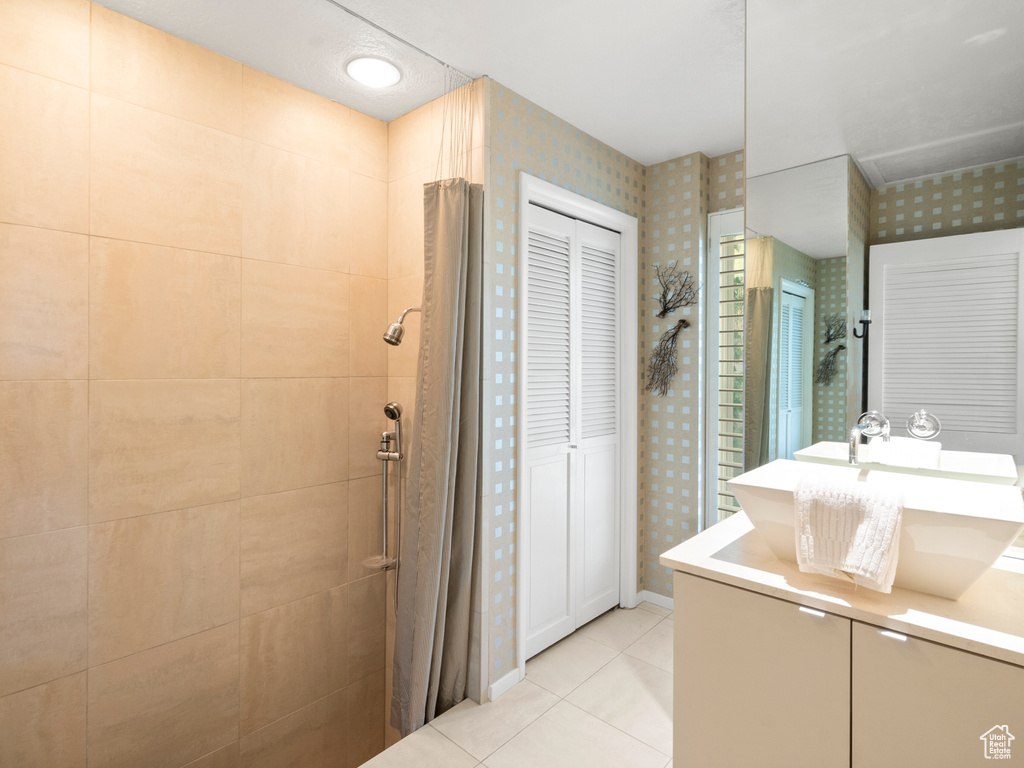 Full bath with wallpapered walls, vanity, tile patterned floors, a tile shower, and a closet