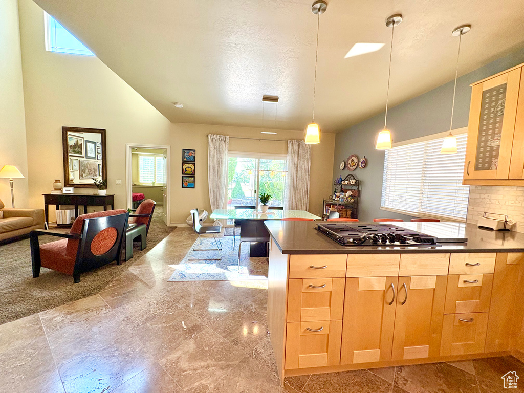 Kitchen with gas stovetop, vaulted ceiling, light brown cabinetry, dark countertops, and glass insert cabinets