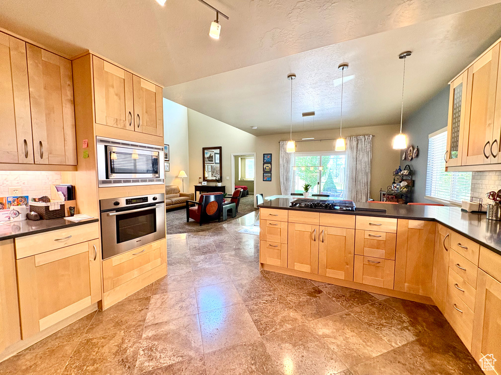 Kitchen with light brown cabinets, appliances with stainless steel finishes, and vaulted ceiling