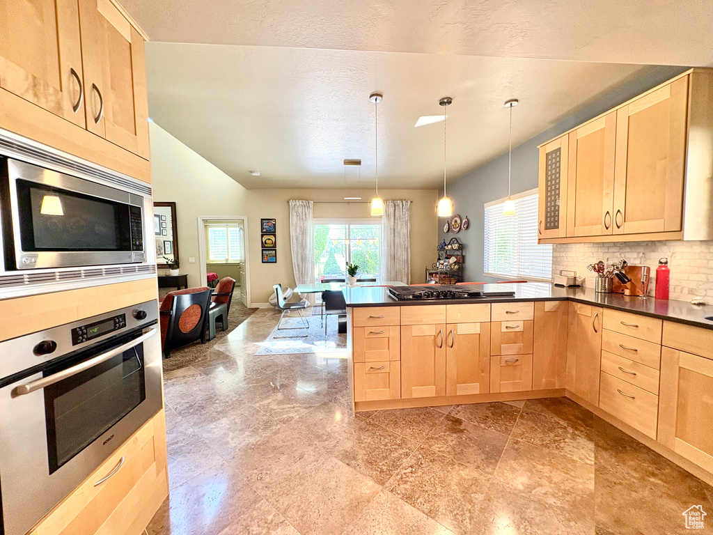 Kitchen with light brown cabinetry, appliances with stainless steel finishes, dark countertops, a peninsula, and vaulted ceiling