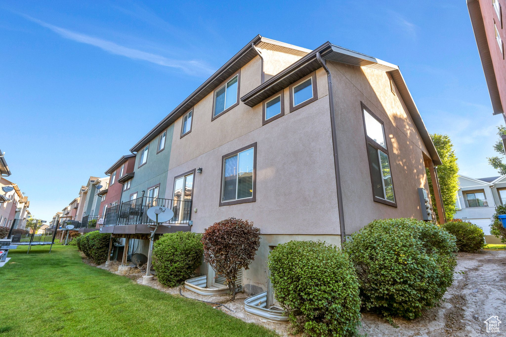 View of property exterior with a trampoline, stucco siding, a yard, a residential view, and a balcony