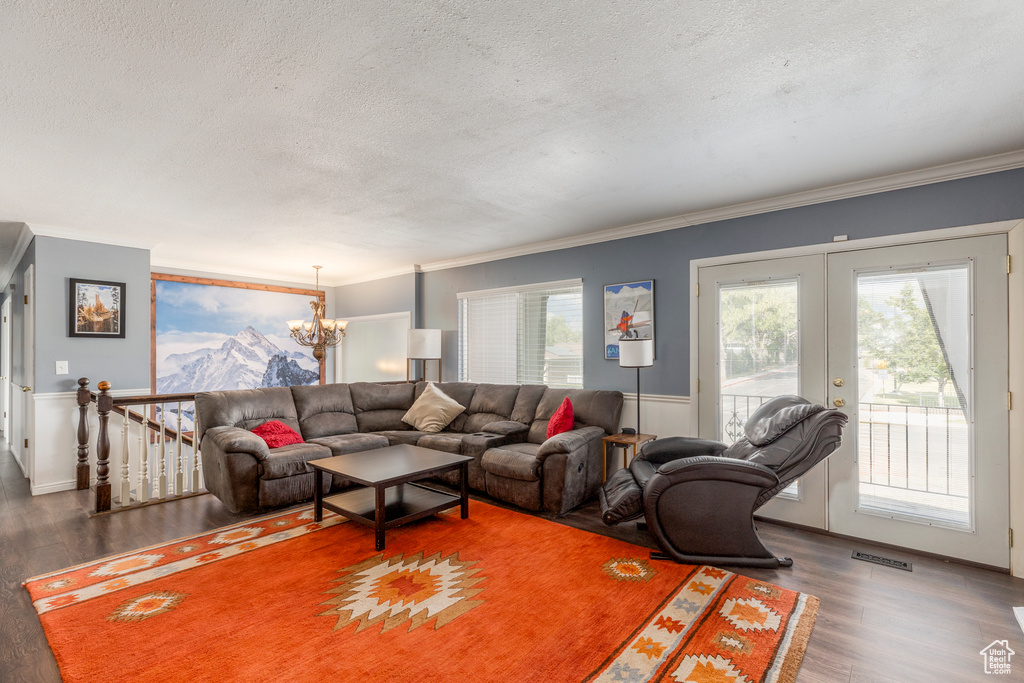 Living room featuring a textured ceiling, a chandelier, wood finished floors, ornamental molding, and french doors