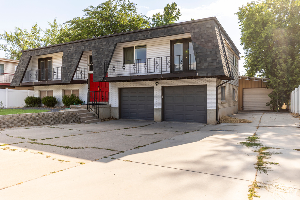 View of front of home featuring brick siding, a garage, a balcony, driveway, and mansard roof