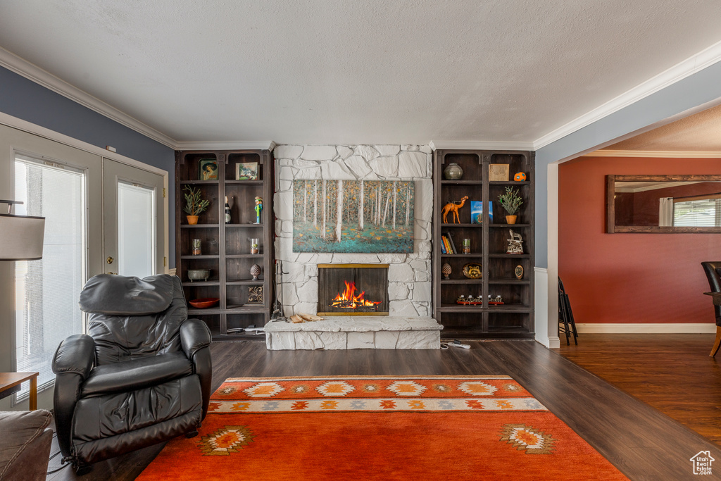 Living area with wood finished floors, a stone fireplace, and crown molding