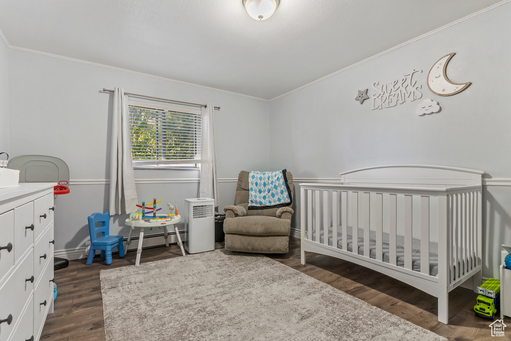 Bedroom with a baseboard heating unit, ornamental molding, dark wood-type flooring, and a crib