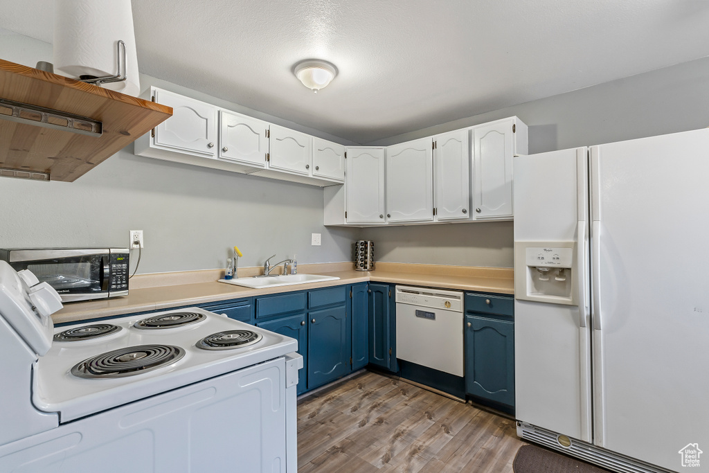 Kitchen with white appliances, blue cabinetry, light wood-style floors, and white cabinetry
