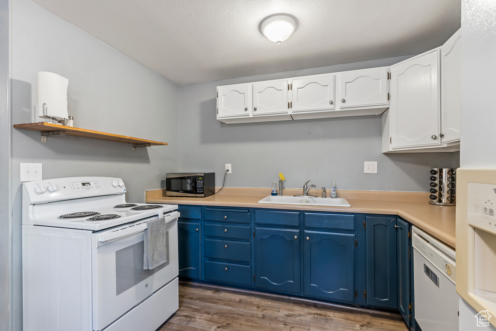 Kitchen with white appliances, blue cabinets, open shelves, white cabinets, and wood finished floors