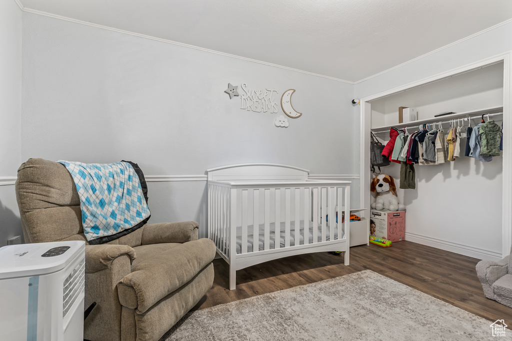 Bedroom with wood finished floors, crown molding, a nursery area, and a closet