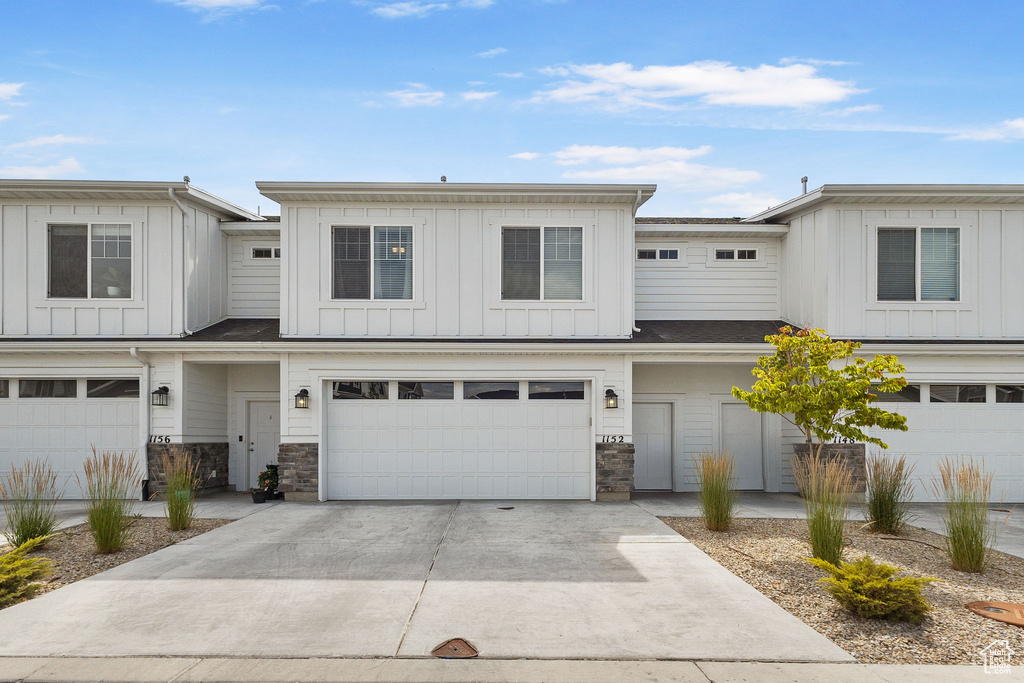 Townhome / multi-family property with board and batten siding, an attached garage, concrete driveway, and stone siding