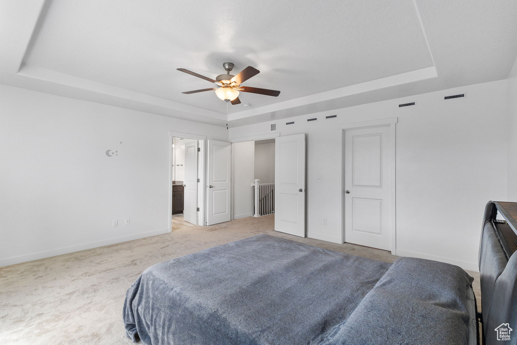 Bedroom featuring a tray ceiling, carpet flooring, ensuite bath, and a ceiling fan