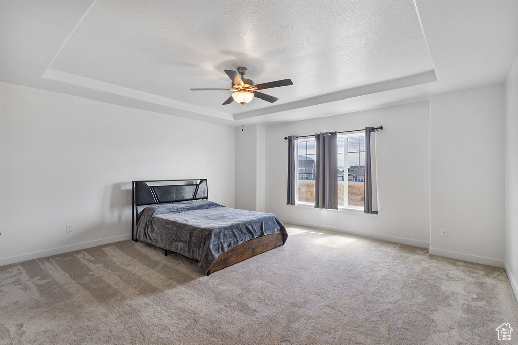 Bedroom featuring a raised ceiling, carpet floors, and a ceiling fan