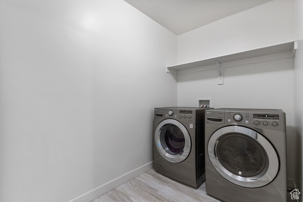 Laundry room with washer and clothes dryer and light wood-style floors