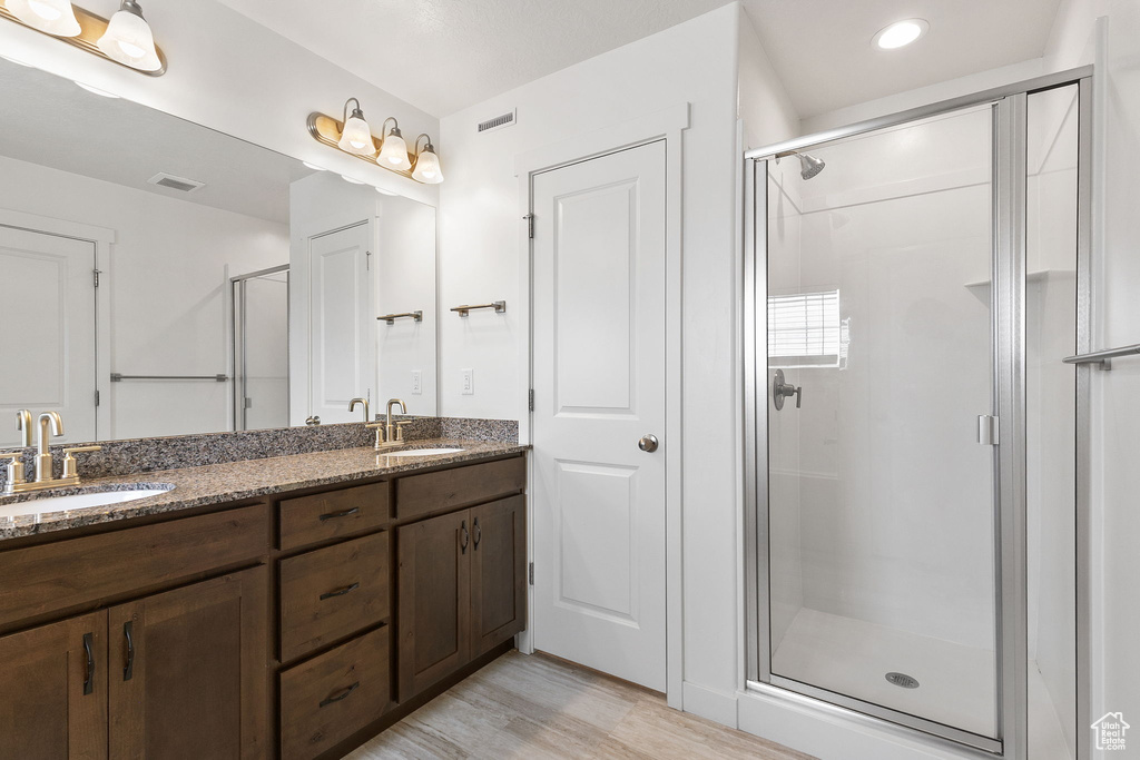 Bathroom featuring a shower stall, double vanity, wood finished floors, and recessed lighting