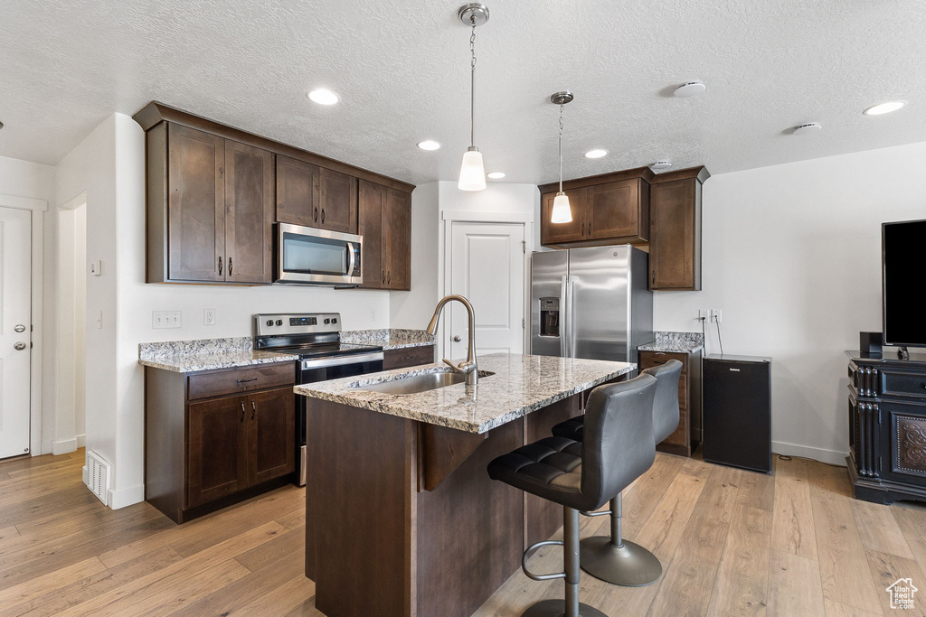 Kitchen featuring stainless steel appliances, dark brown cabinets, a breakfast bar area, light wood finished floors, and a textured ceiling
