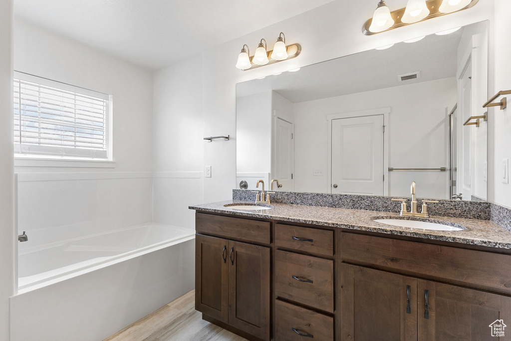 Bathroom with double vanity, a bath, and wood finished floors